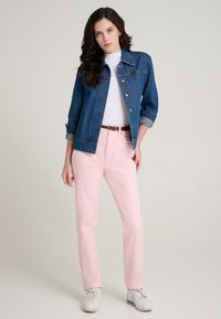 Giacca di jeans con chiusura a bottoni, lavaggio chiaro e maniche risvoltate abbinata a pantaloni rosa a gamba dritta. Scarpe da ginnastica bianche completano il look.