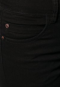 Svarta denimjeans med en närbild på midjebandet, fickan med kopparnitar och tonalt sömnad för en slät textur.