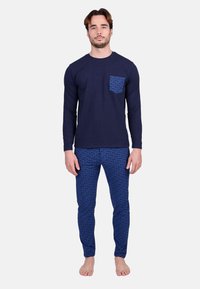 Chemise à manches longues marine avec une poche à motifs, associée à un pantalon bleu à motifs présentant un design de logo. Matériau en coton, style ajusté.