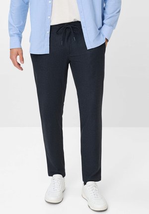 Pantalons gris foncé avec une taille à cordon, texture lisse et design à jambes fuselées, associés à des baskets blanches et une chemise à boutons bleu clair.