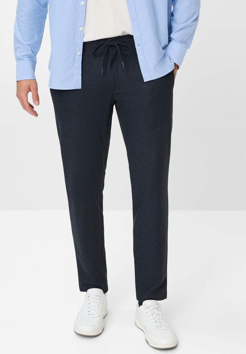 Dunkelgraue Hose mit Kordelzugbund, glatter Textur und schmal zulaufendem Bein, kombiniert mit weißen Sneakern und einem hellblauen Hemd mit Knöpfen.