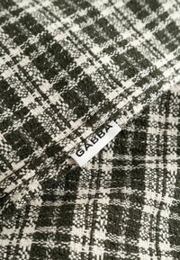 Gros plan d'un tissu tissé noir et blanc à motif à carreaux avec une petite étiquette blanche portant la mention "GABBA", cousue sur le bord.