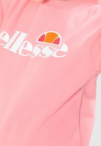 Růžová mikina vyrobená z měkké tkaniny, s bílým logem "ellesse" a vícebarevným akcentem v oranžové, žluté a bílé nad logem.