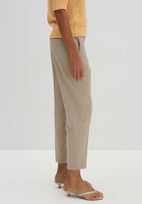 Beige Hochbundhosen mit geradem Bein, die über eine glatte Textur, seitliche Taschen und eine cropped Länge verfügen. Kombiniert mit einfachen Sandalen.