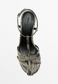 Ormskinn högklackad sandal i grå och svarta nyanser. Remdesign med ankelspänne, öppen tå och en slät svart innersula.