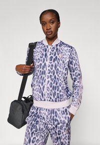 Survêtement à imprimé léopard en nuances de violet et rose, comprenant une veste zippée et une taille élastique, accompagné d'un sac noir.
