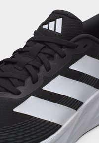 Μαύρο αθλητικό παπούτσι Adidas με λευκές τρεις ρίγες, μαύρα κορδόνια και μαλακή λευκή σόλα.