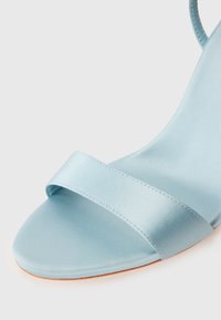Svetlomodré saténové sandále so širokým remienkom cez prsty a hladkým, zakriveným opätkom. Lesklý povrch, minimalistický dizajn. Plochá podrážka.