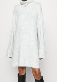 Abito maglione lungo a maniche lunghe di un grigio chiaro, con collo alto, texture a coste e polsini oversize. Realizzato in morbido materiale in maglia, design fino al ginocchio.