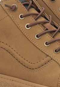 Bruine suède schoenen met metalen oogjes, bruine veters en contrasterende stiksels. Heeft een zachte textuur en een rond ontwerp.
