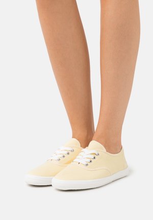 Baskets en toile jaunes avec lacets blancs, bout rond et tissu texturé. Semelle en caoutchouc avec des accents de couture, design décontracté.