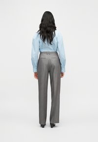 Chemise bleu clair à manches longues bouffantes, associée à un pantalon gris sur mesure. La tenue présente une silhouette nette et structurée.