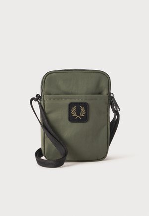 Sac bandoulière compact vert olive avec sangle réglable noire et poche avant ornée d’un écusson noir avec un emblème de couronne de laurier dorée.