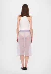 Průsvitná fialová sukně s elastickým pasem, vrstvený design a boční rozparek, nošená přes bílý top na ramínka a černou obuv.