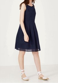 Námořnické šaty bez rukávů s záhyby, vyrobené z lehké tkaniny. Spárované s bílými espadrilkami s tkaným designem a kotníkovými šňůrkami.