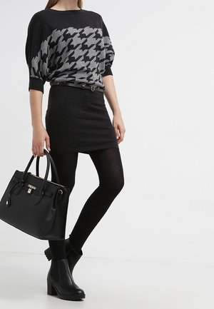 Zwart houndstooth-patroon trui over een nauwsluitende zwarte rok, gecombineerd met zwarte maillots en enkellaarzen. Inclusief een zwarte handtas met gouden hardware.