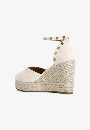 Beige wedge espadrille with a textured suede upper, ankle strap featuring decorative gold studs, and natural rope-wrapped heel.