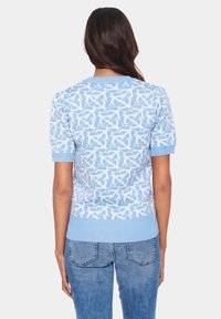 Modrý pletený svetr s bílým abstraktním vzorem, žebrovanými lemy a spodním okrajem, krátkými rukávy a klasickým kulatým výstřihem.