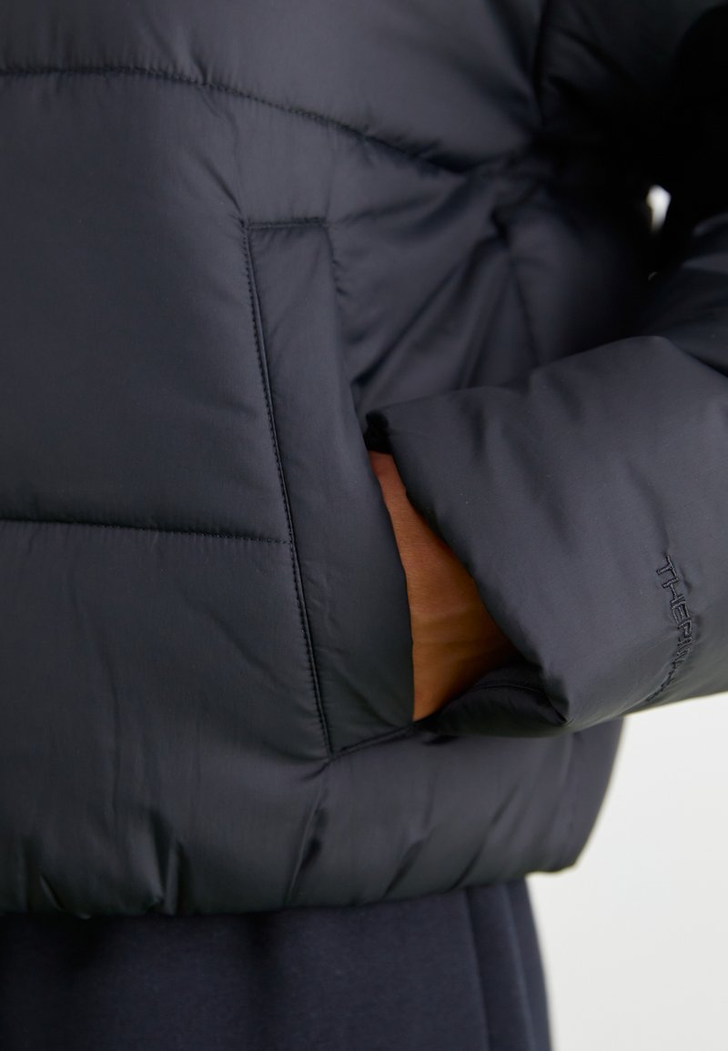 Giacca a vento nera con design trapuntato, texture morbida, tasca laterale e cuciture a contrasto, realizzata in materiale leggero.