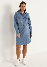 Jeansklänning, ljusblå, knappupp, långa ärmar, två bröstfickor, rak passform, mjukt material, bärs med vita sneakers.
