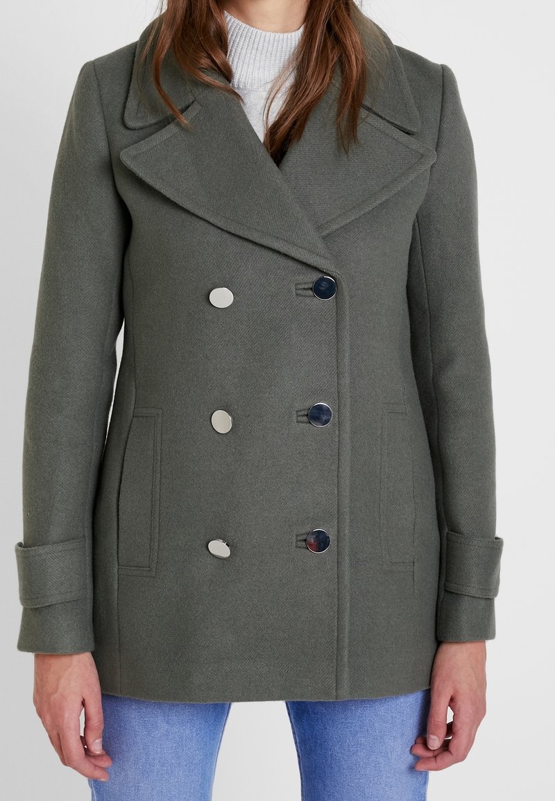 Abrigo de lana verde de doble botonadura con grandes solapas, botones plateados y bolsillos laterales. Presenta una tela texturizada y un ajuste entallado.