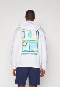 Biela mikina s viacerými farebnými geometrickými vzormi na chrbte s textom "SPORTIVAMENTE." Mäkko tkané a vo voľnom strihu.