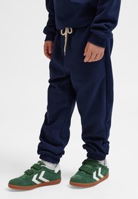 Granatowe dresowe spodnie z bawełny z elastycznymi mankietami i sznurkiem w pasie; połączone z zielonymi trampkami z białymi akcentami i zapięciem na rzepy.