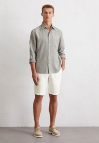 Hellgrau gestreifte Langarmbluse, weiße Shorts und beigefarbene Schuhe. Das Hemd hat einen Button-Down-Kragen und eine Brusttasche.