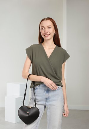 Olijfgroene wikkeltop, spijkerbroek en een zwarte handtas in hartvorm met een gouden rits. Gladde stof, casual ontwerp en verstelbare riem.