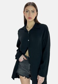 Schwarzes Hemd zum Knöpfen aus strukturiertem Stoff, mit lockerem Schnitt, langen Ärmeln und einem Reverskragen, kombiniert mit zerstörten Jeansshorts.