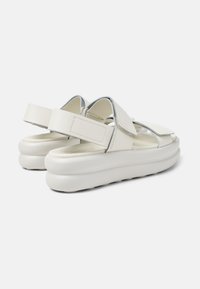 Vita plattformssandaler med texturerade remmar, justerbara Velcro-stängningar och rundade sulor, med en slät yta och minimalistisk design.