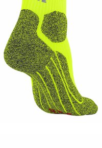 Calzino atletico imbottito giallo neon e nero, teso su un piede, con aree visibili di supporto imbottito per il tallone, la soletta e l'arco.