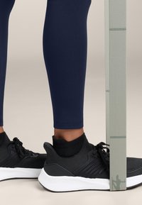 Pantofi sport negri cu talpă albă, purtați cu colanți navy, având un design texturat și șosete negre până la glezna. Banda de tensiune se află lângă picior.