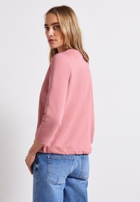 Ljusrosa sweatshirt med trekvartsärmar, rundad halsringning och ribbade mudd. Bärs med ljusblå, högmidjade jeans.