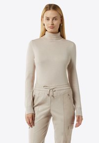 Beige Rollkragenpullover aus weichem, geripptem Material, kombiniert mit cremefarbenen Jogginghosen mit elastischem Bund und Reißverschlusstaschen.