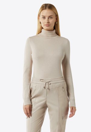 Beige Rollkragenpullover aus weichem, geripptem Material, kombiniert mit cremefarbenen Jogginghosen mit elastischem Bund und Reißverschlusstaschen.