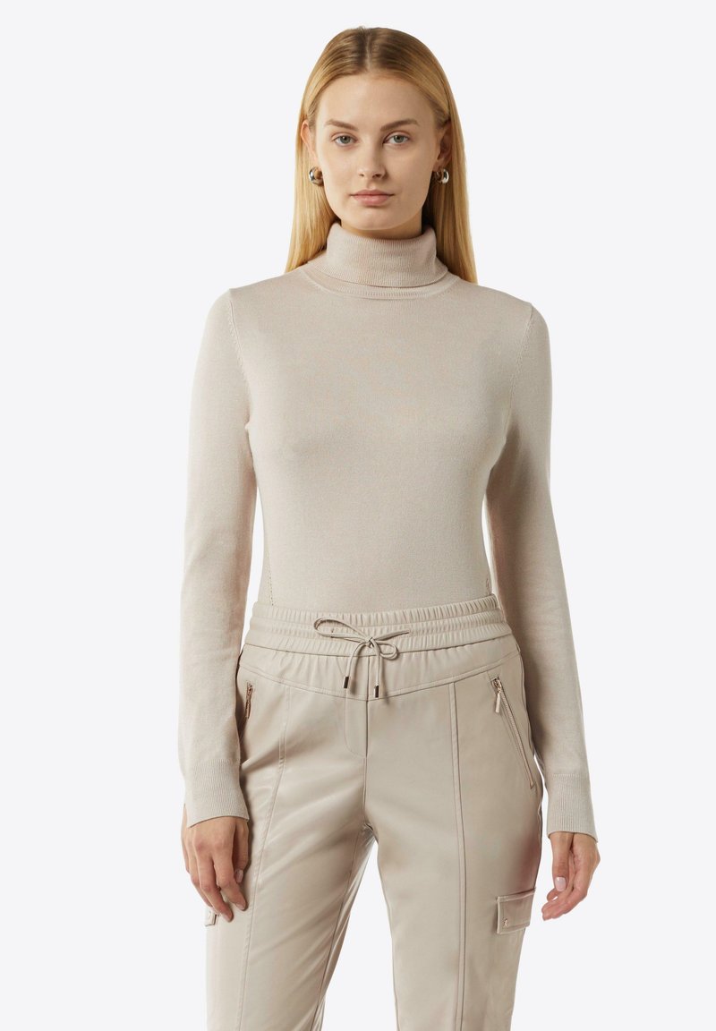 Beige Rollkragenpullover aus weichem, geripptem Material, kombiniert mit cremefarbenen Jogginghosen mit elastischem Bund und Reißverschlusstaschen.