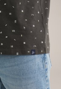 Sort bomulds t-shirt med spredte lys farvede lodrette striber; har et lille marineblåt mærke ved kanten. Sammen med blå denim.