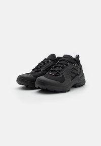 Czarne buty sportowe z oddychającą siateczką, teksturowaną gumową podeszwą, wzmocnionym czubkiem i solidnym systemem sznurowania zapewniającym pewne dopasowanie.