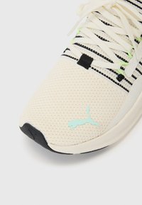 White mesh athletic shoe featuring black and green stripes, a black sole, and a light blue logo on the side. Textured upper for breathability.