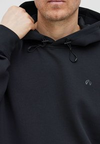 Svart hooded sweatshirt med en slät textur, med justerbara snören och en liten logotyp på bröstet.
