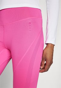 Roza atletska legginga iz raztegljive tkanine, ki se ponaša z gladko teksturo, diskretni vzorec in logotipom na levi strani. Poglej od blizu.