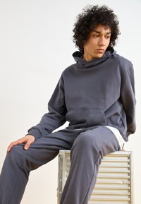 Grå hettegenser og matchende joggebukser laget av myk stoff; har en kengurulomme, avslappet passform og ribbestrikkede mansjetter. Enkel design uten mønstre.