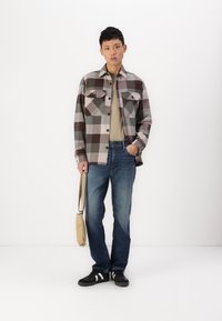 Rutet flanellskjorte i brun, beige og grå, med to brystlommer, kombinert med en beige t-skjorte og blå denimjeans. Svarte sneakers og en lys brun veske.