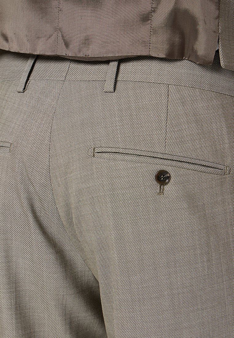 Un pantalon tailored gris clair présente une texture en chevron, une poche arrière unique avec fermeture à bouton et des coutures soignées le long des coutures.