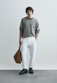 Szürke pulóver zsebbel, fehér, szűkített nadrág, fekete cipő és barna bevásárlótáska. Sima textúra, laza szabás, semleges árnyalatok.