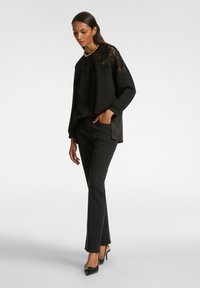 Top negro con detalles de encaje en los hombros, combinado con pantalones negros con estampado y tacones negros. Tela suave con un ajuste relajado.