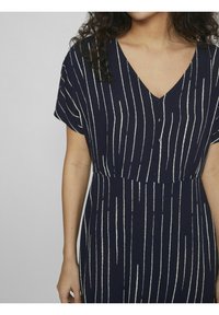 Mekko, jossa on valkoisia pystyraitoja, V-maallinen kaula-aukko, lyhyet hihat ja etupainanta; kevyt kangas ja istuva vyötärö.