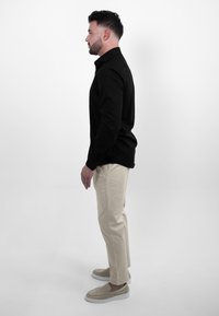 Zwart lang mouw shirt, beige chinos en grijze instappers. Profielweergave, gladde stof, perfecte pasvorm, eenvoudig ontwerp en neutrale kleuren.