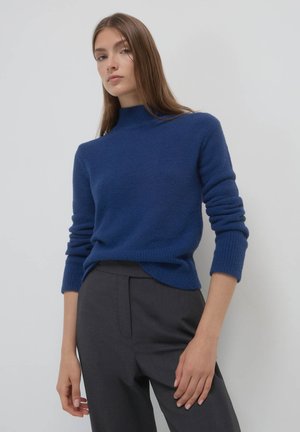 Blauer Pullover mit hohem Kragen, strukturiertem Strickstoff und langen Ärmeln, kombiniert mit grauen, maßgeschneiderten Hosen. Einfaches und sauberes Design.